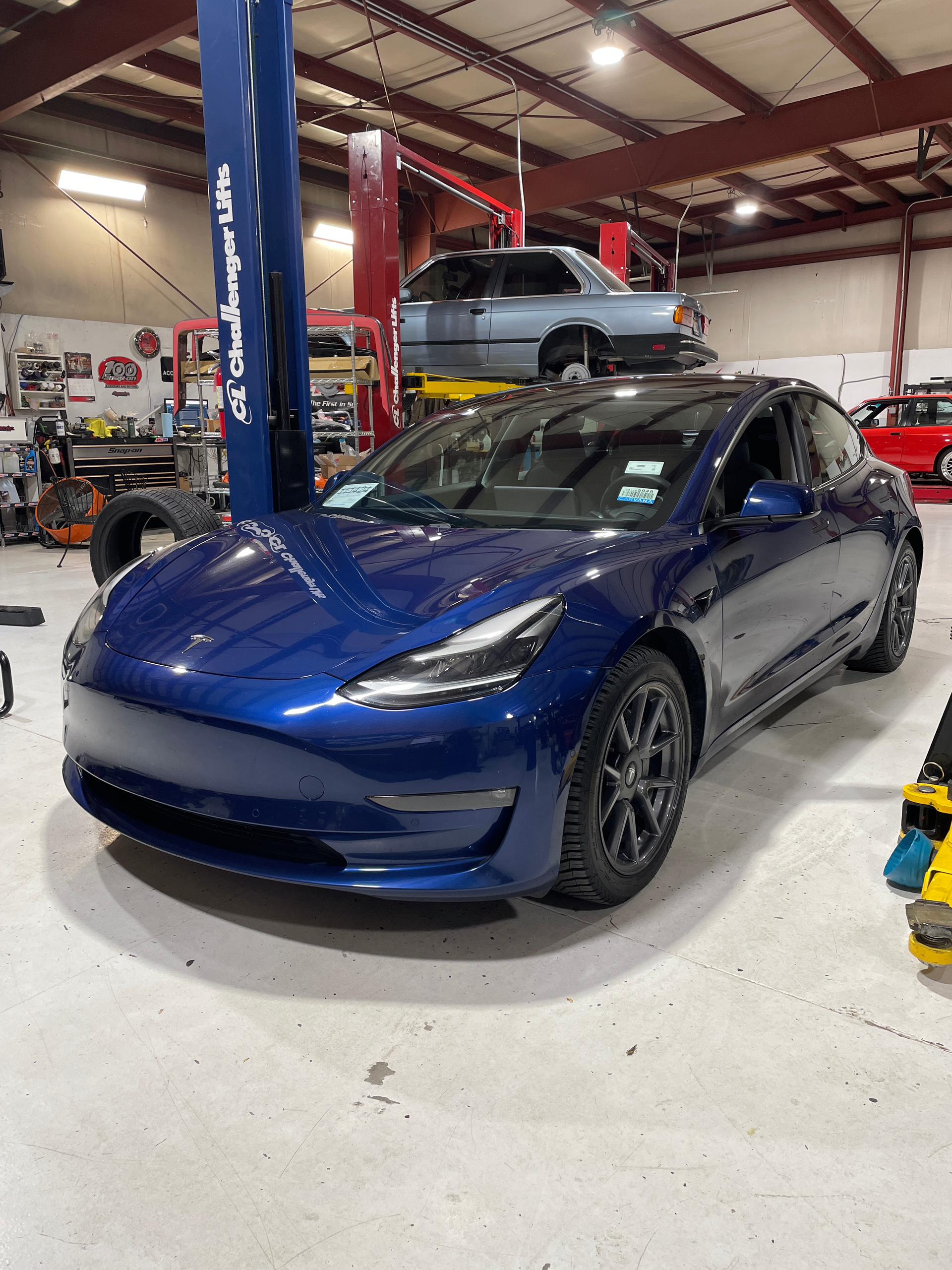 A blue tesla model 3 is on a lift in a garage.