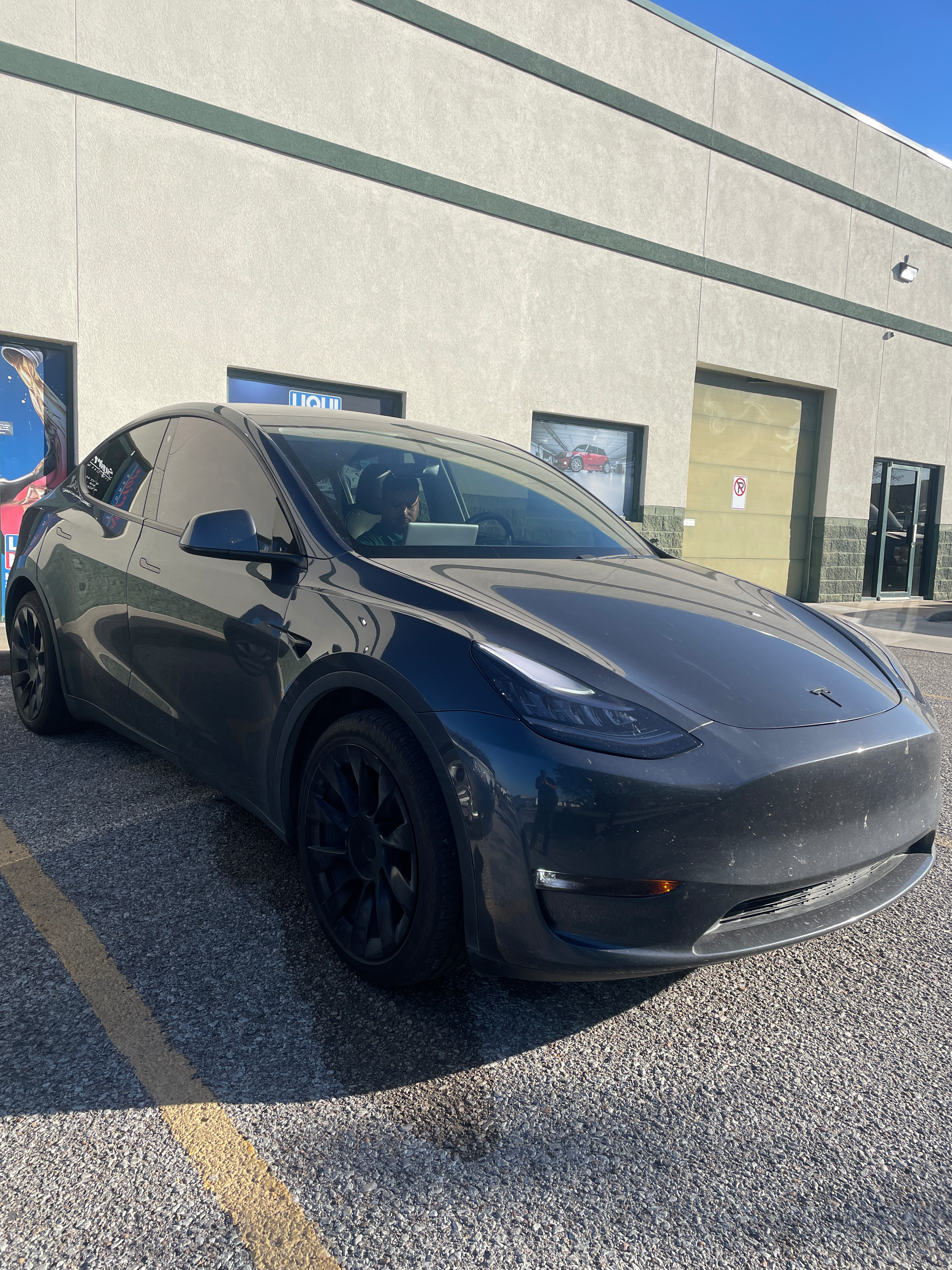A black tesla model y is parked in front of a building.