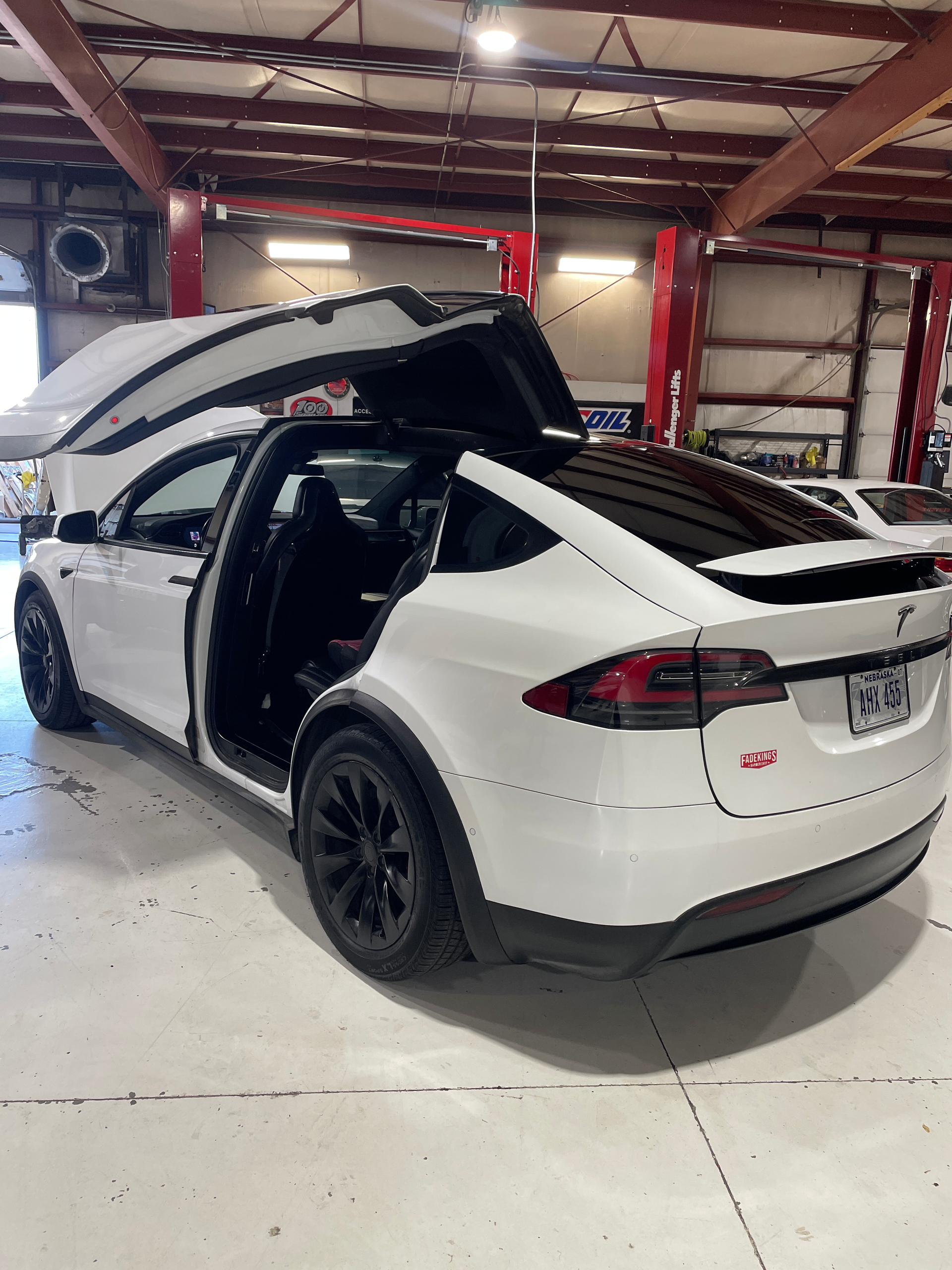 A white tesla model x is parked in a garage with its trunk open.