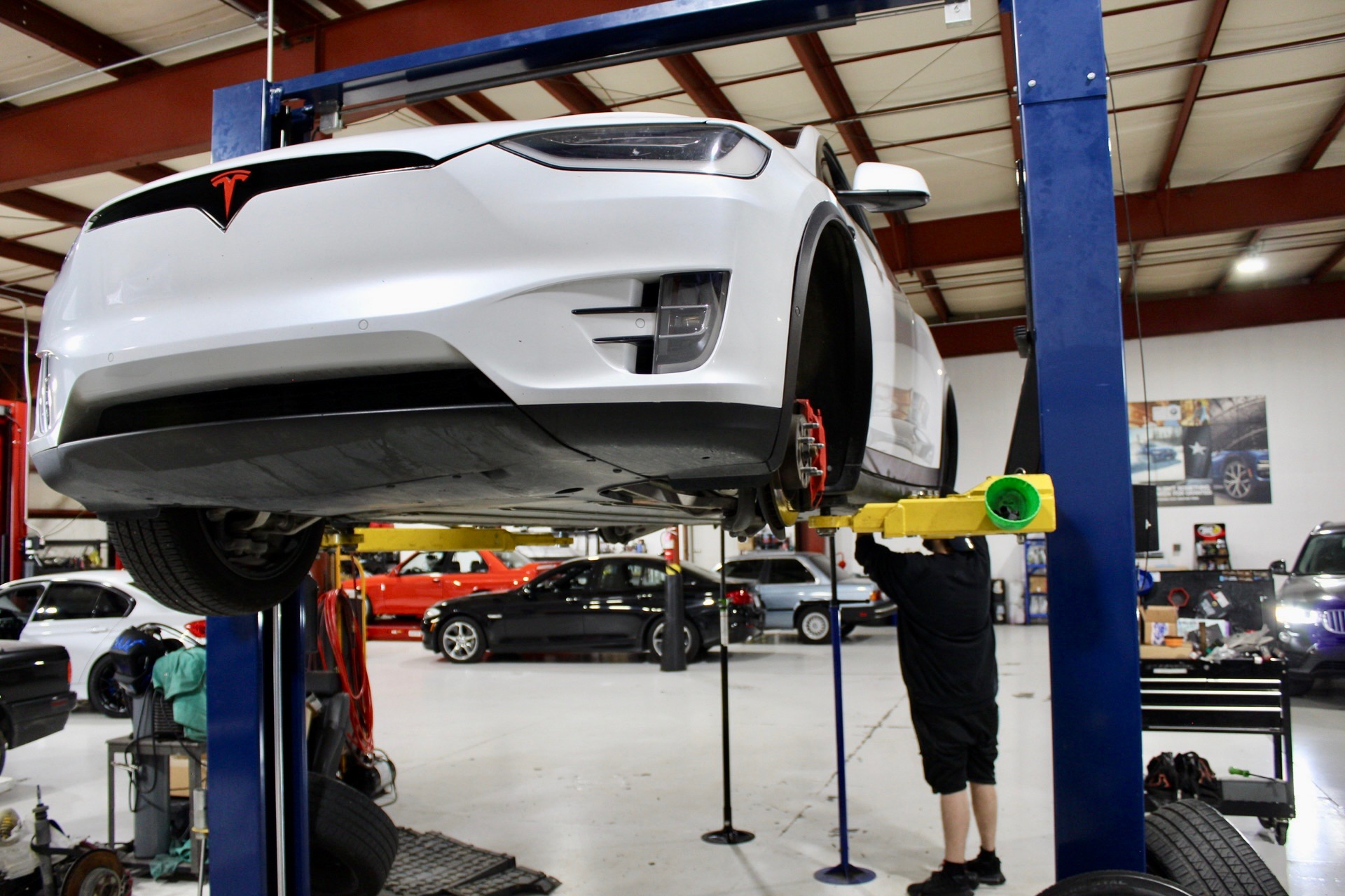 A man is working on a tesla model x on a lift in a garage.