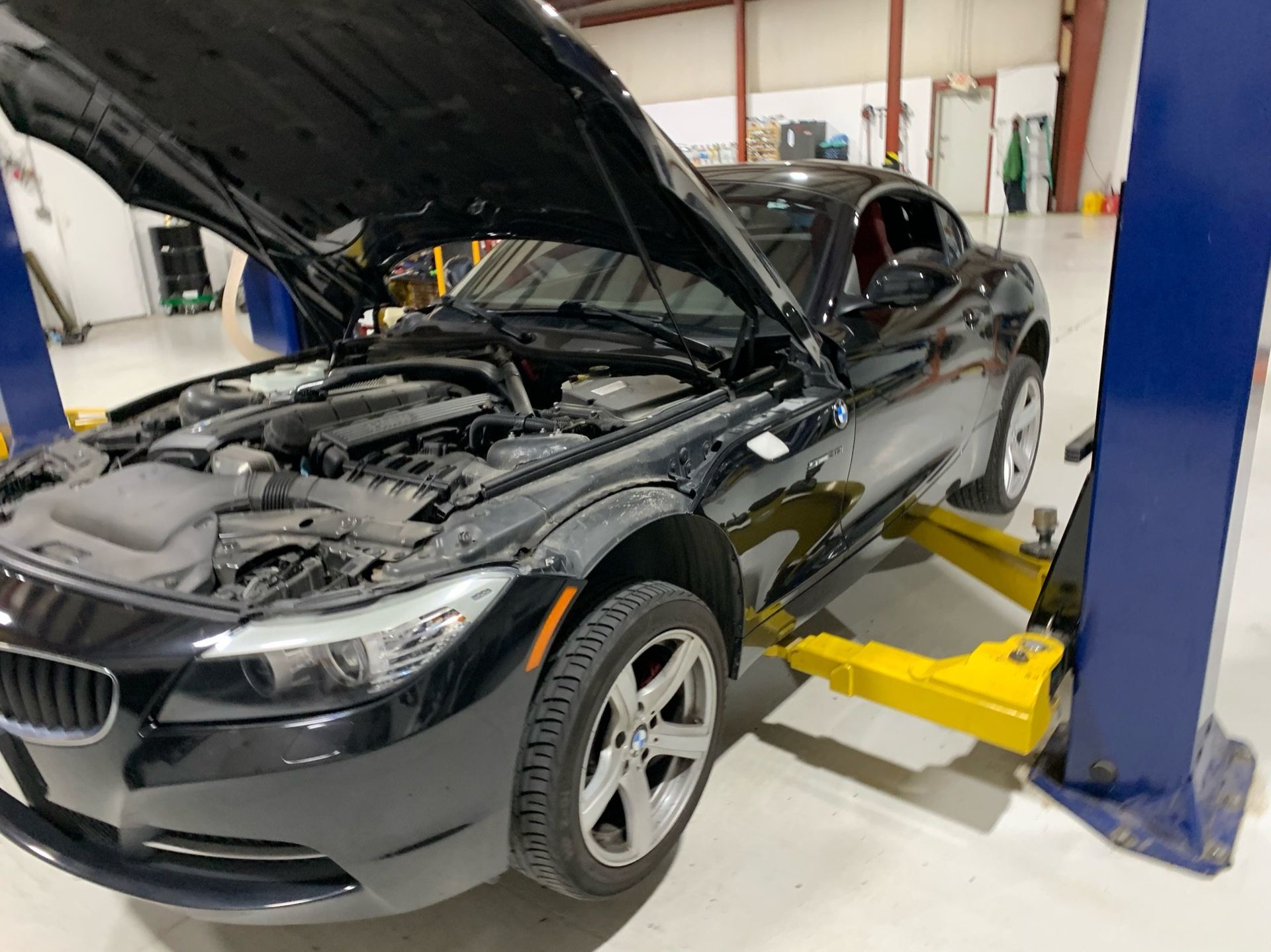 a black car with the hood up is on a lift in a garage 