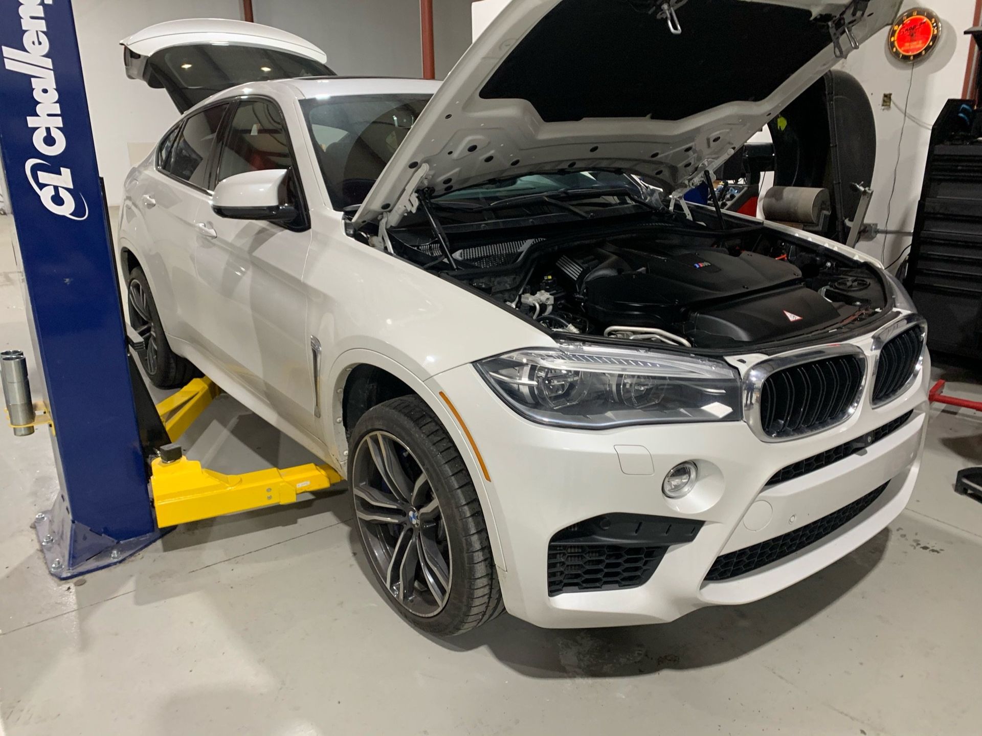 a white bmw x6 m is sitting on a lift with its hood open 