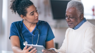 A nurse is speaking to an elderly man in a wheelchair.