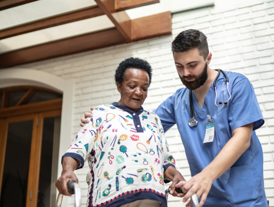 A nurse is helping an elderly woman walk with a walker.