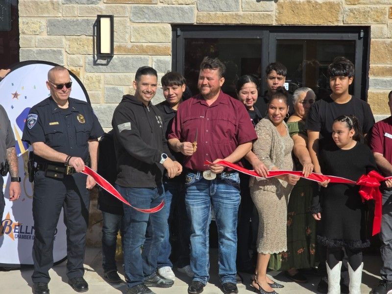 A group of people are cutting a red ribbon in front of a building.
