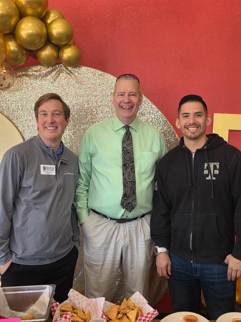 Three men are posing for a picture in front of a table of food.