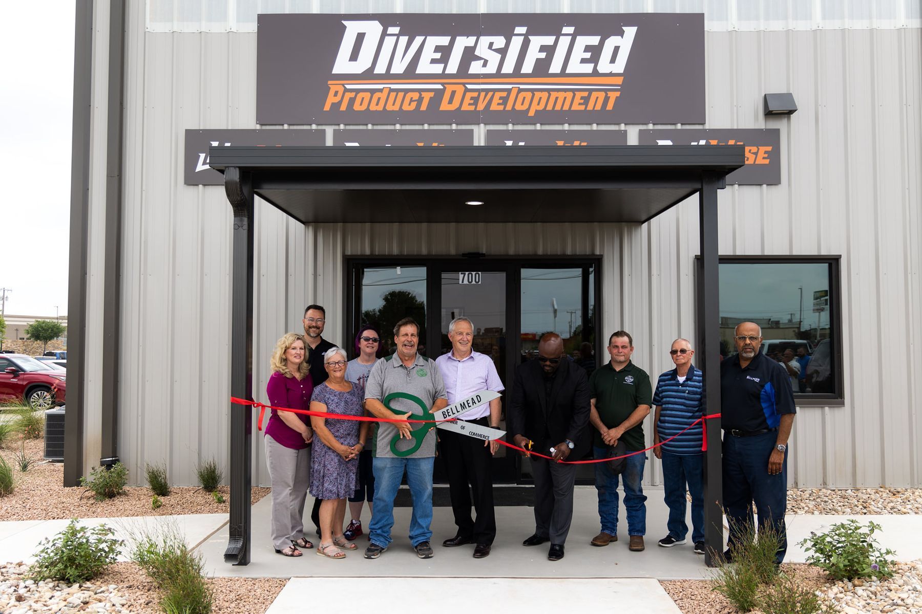 A group of people are cutting a red ribbon in front of a building.