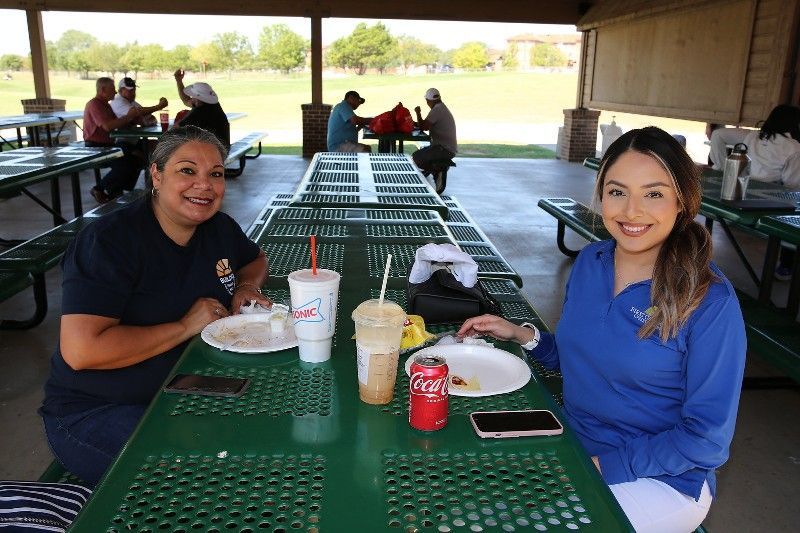Two women are sitting at a picnic table in a park.