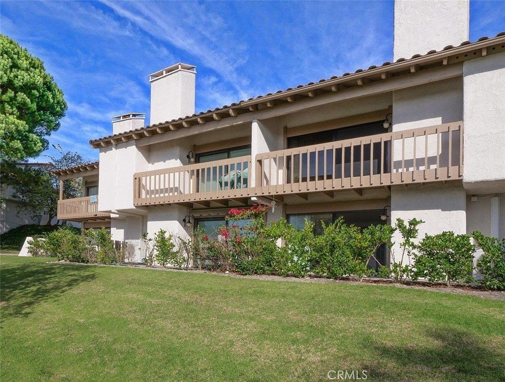 Two-story beige townhouse with balcony, white chimneys, and green lawn under a blue sky