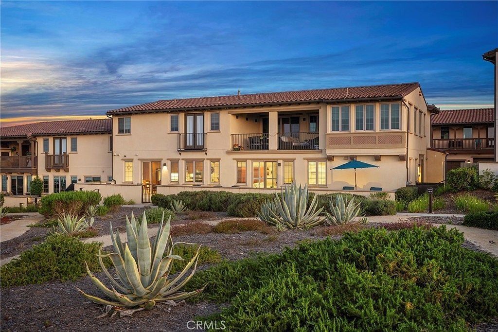 Two-story tan apartment buildings with tiled roofs amid desert landscaping at dusk