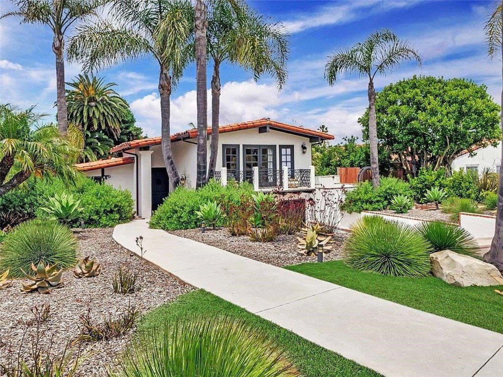 Landscaped home with palm trees, white walkway, and red-tiled roof under a blue sky