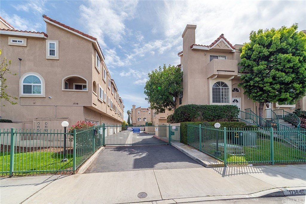 Gated driveway between beige apartment buildings under a bright blue sky