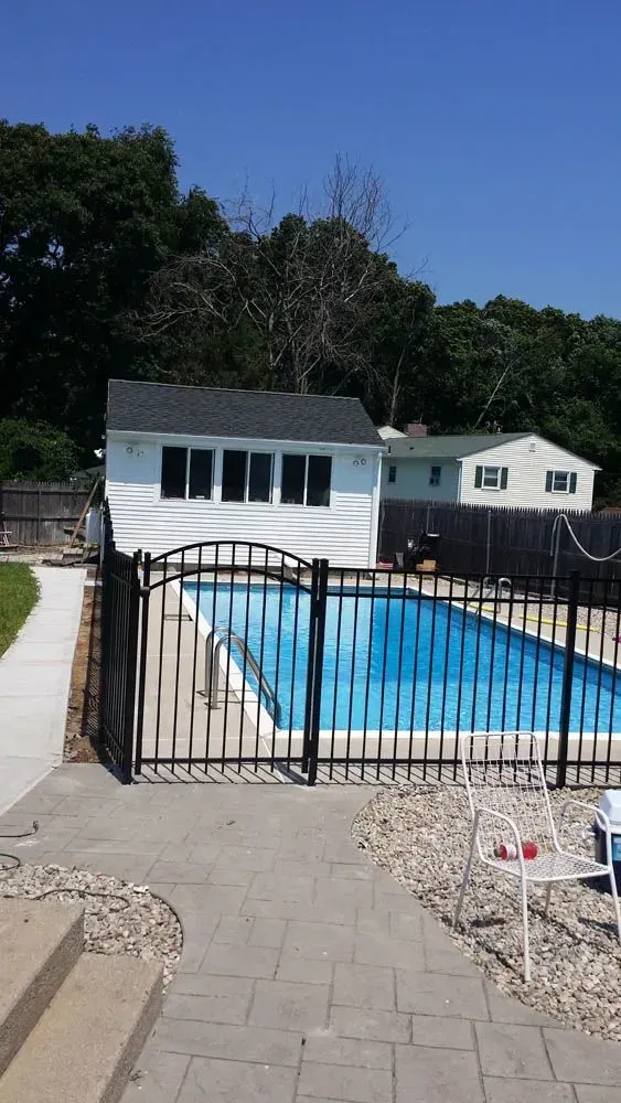 White picket fence curves along a green lawn between two houses, with trees in the background.
