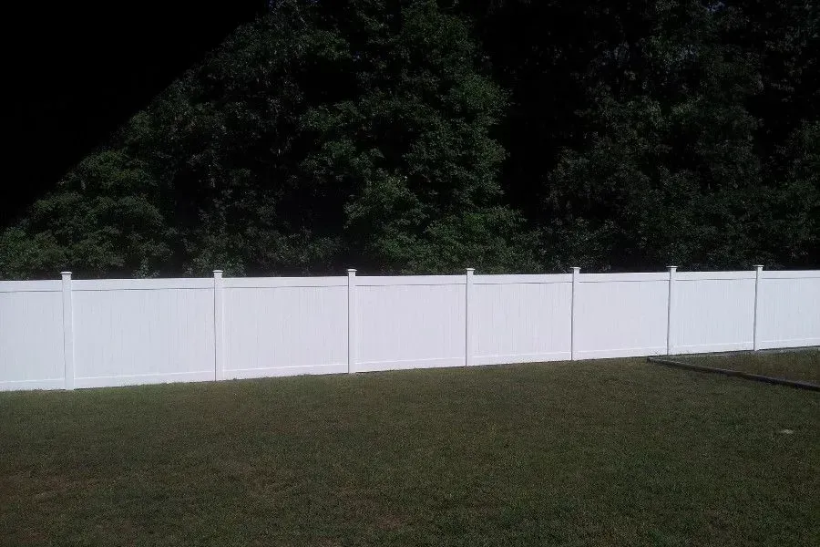 White vinyl fence in a grassy yard, with dark trees in the background.