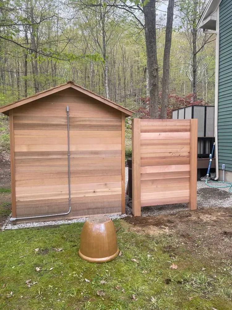 Wooden outdoor shower stall with privacy fence and terracotta pot on grass.