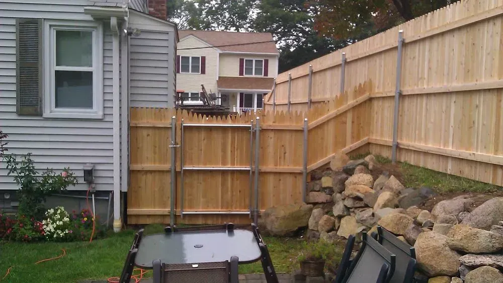 A wooden fence with metal posts is in a backyard near a house. A gate is open with a table in front of it.