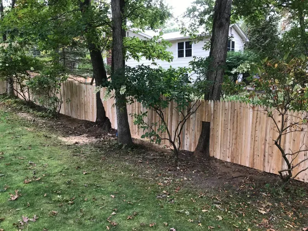 A wooden fence built around trees in a yard with a white house in the background.