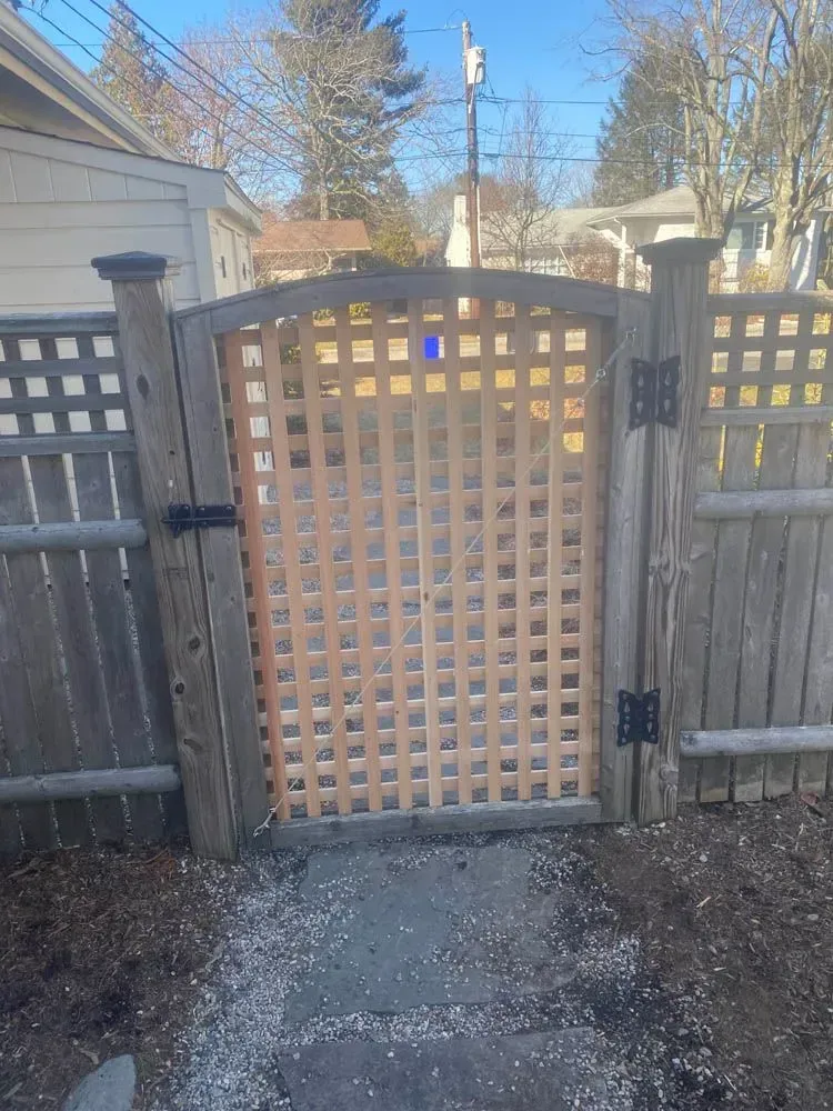 Wooden lattice gate with black hinges and latch set in a wooden fence.
