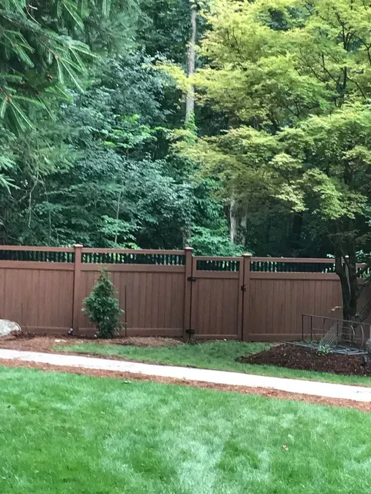 Brown fence with a gate, green lawn, trees in the background.