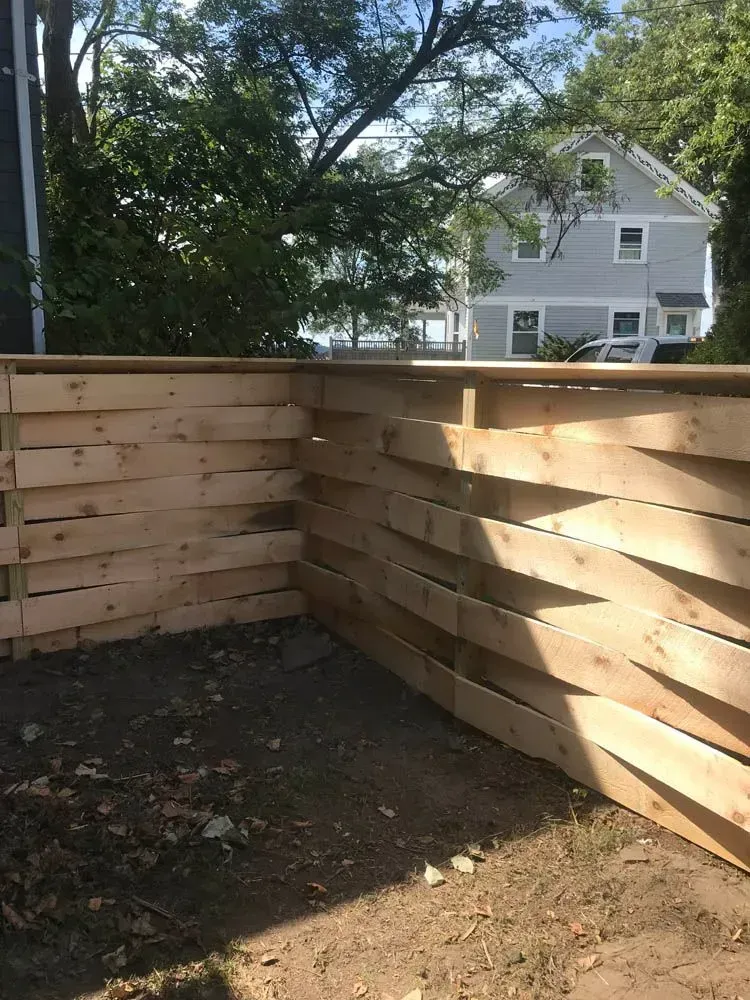 Wooden retaining wall in a yard, built with horizontal planks. A house and trees are in the background.