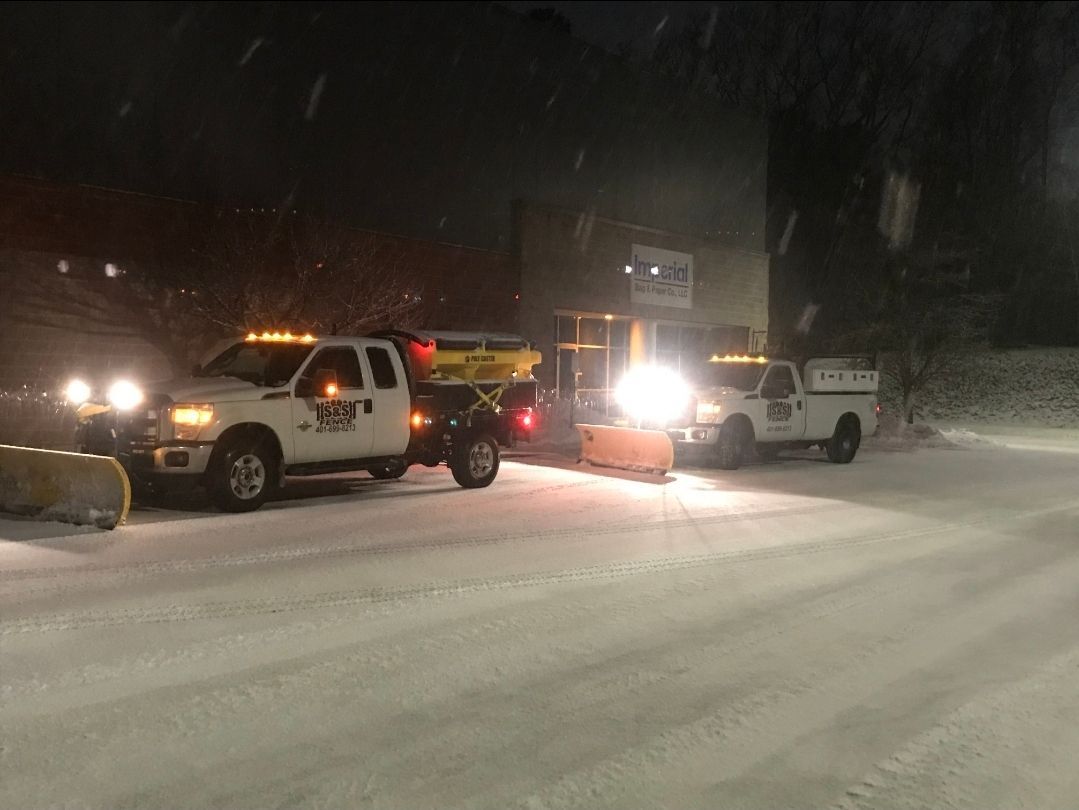 Snowy nighttime roadside with three parked utility trucks and headlights shining