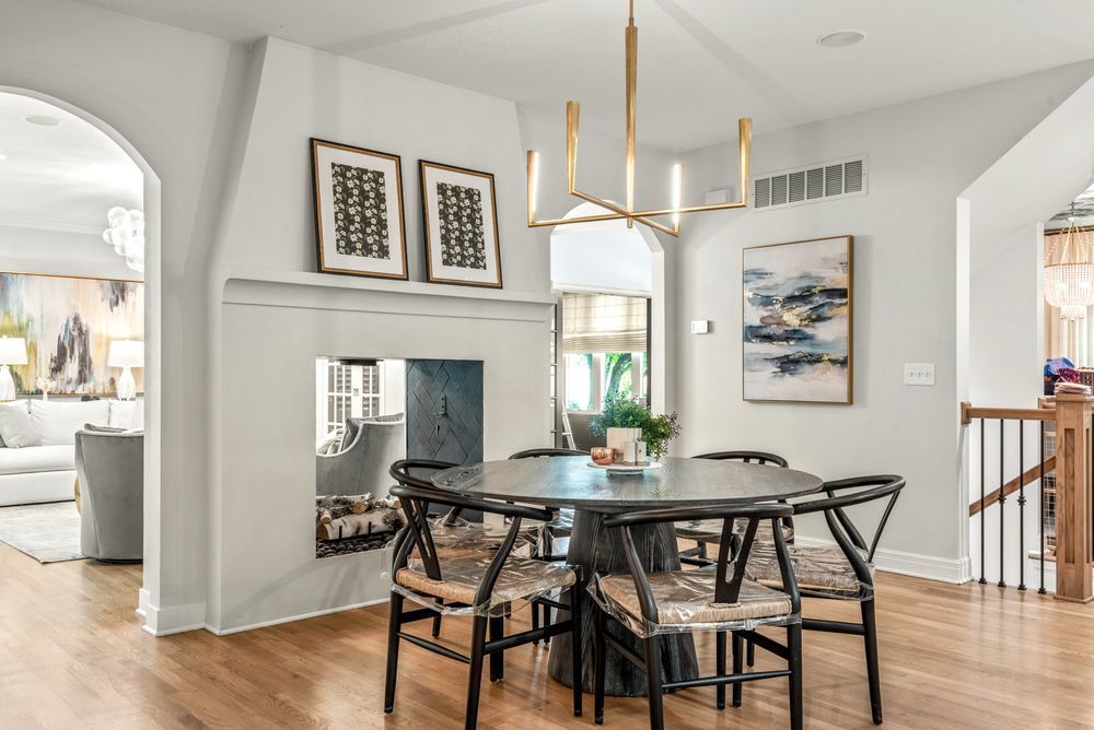 Elegant dining room with a round table and black chairs, a gold chandelier, and artwork. Light-colored walls and hardwood floors.