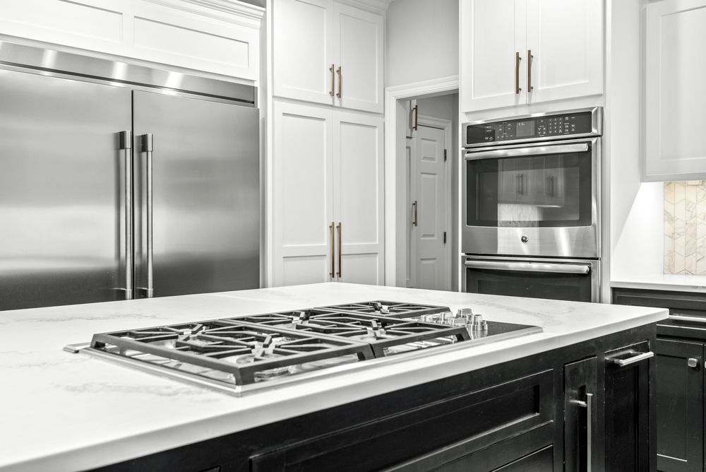 Modern kitchen with a gas cooktop on a white countertop island, stainless steel appliances, and white cabinets.