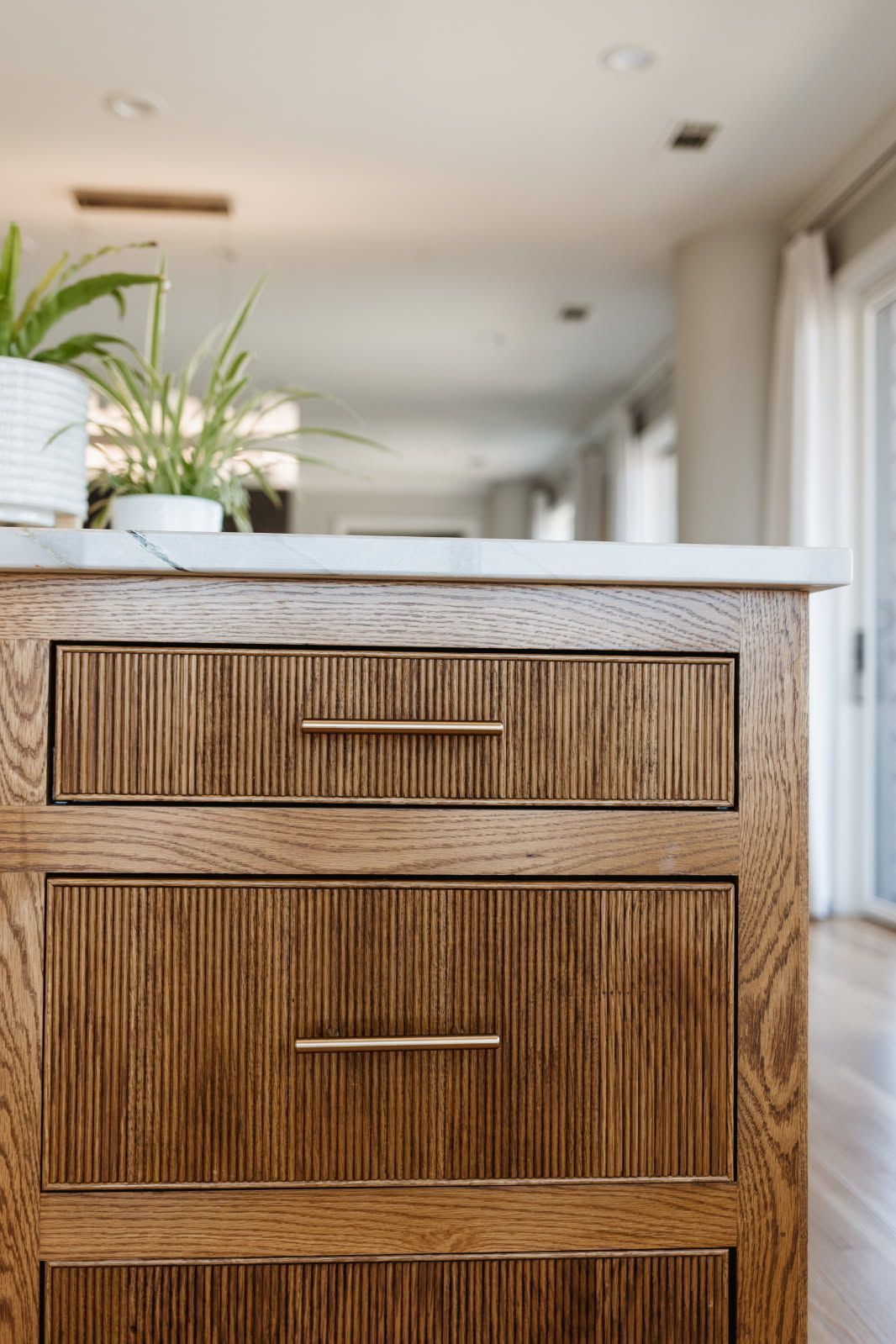 Close-up of a wooden kitchen cabinet with two drawers. The drawers have vertical ribbed texture, brass handles, and a white countertop.