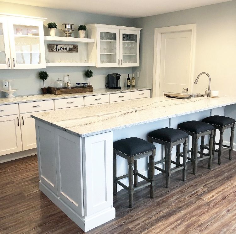White kitchen with a large island, blue walls, and wooden flooring. The island has four dark stools.