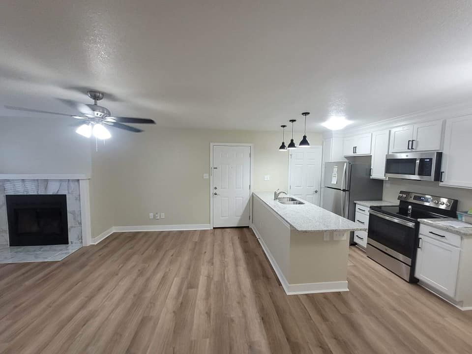 Spacious kitchen with white cabinets and island, stainless steel appliances, and a living area with a fireplace and wooden floors.