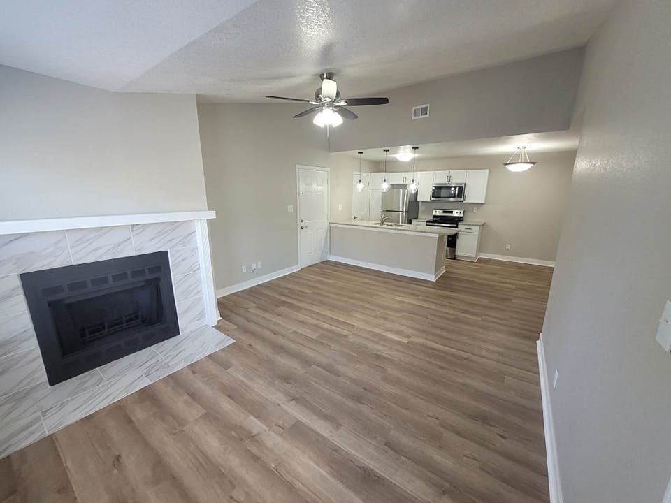 Living room with a fireplace, open to a kitchen. Gray walls, wood-look floors, and white cabinets.