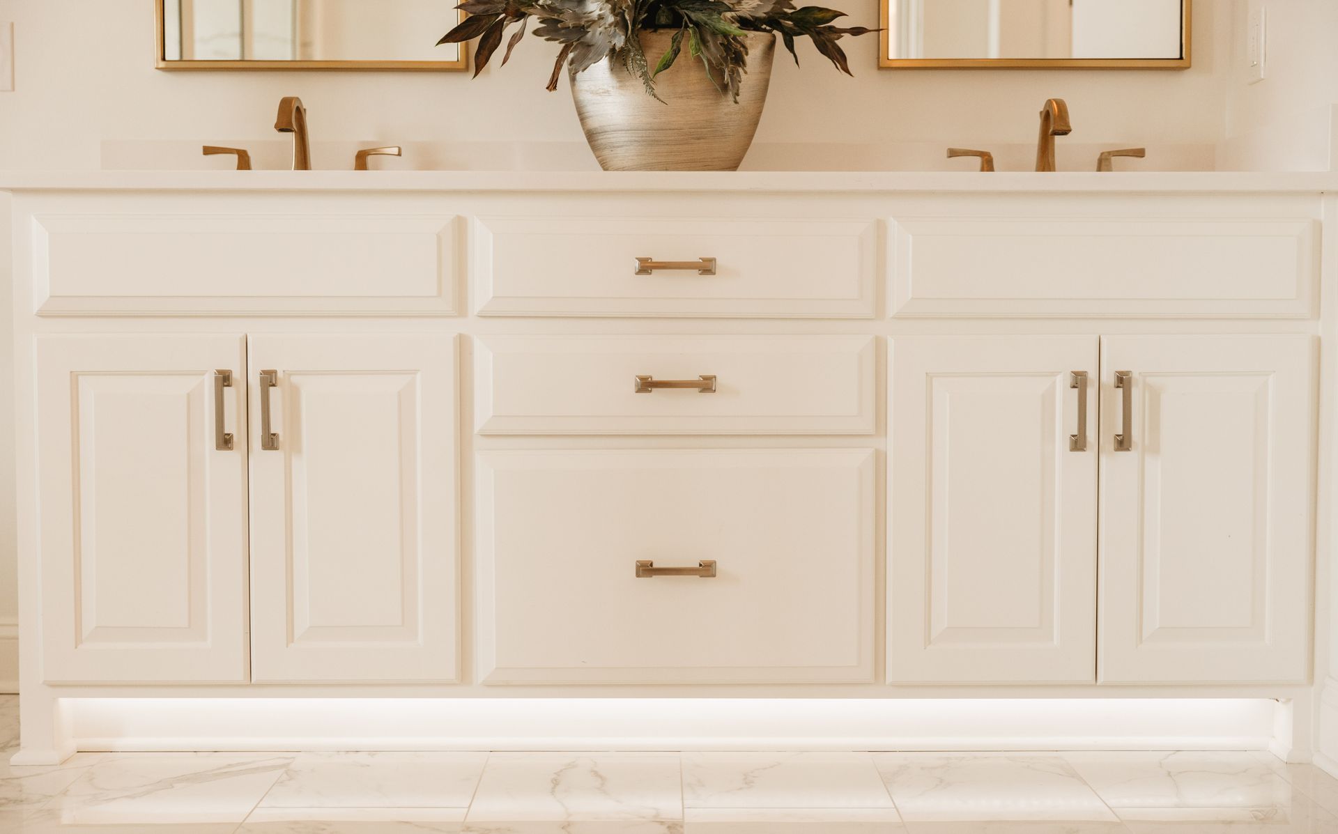 Bathroom vanity with white cabinets, gold fixtures, and floral arrangement