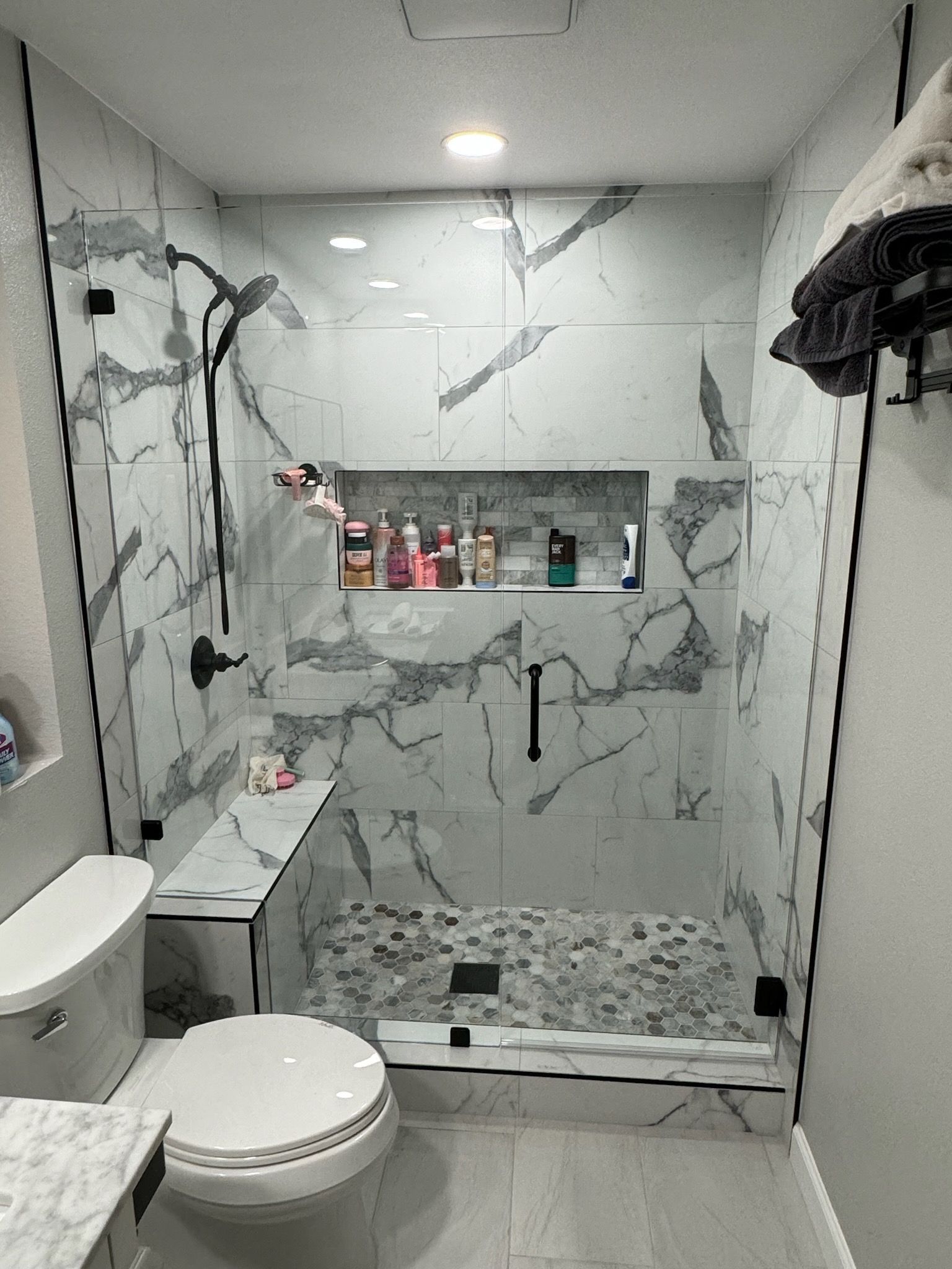 A bathroom with a toilet , shower , and marble tiles.