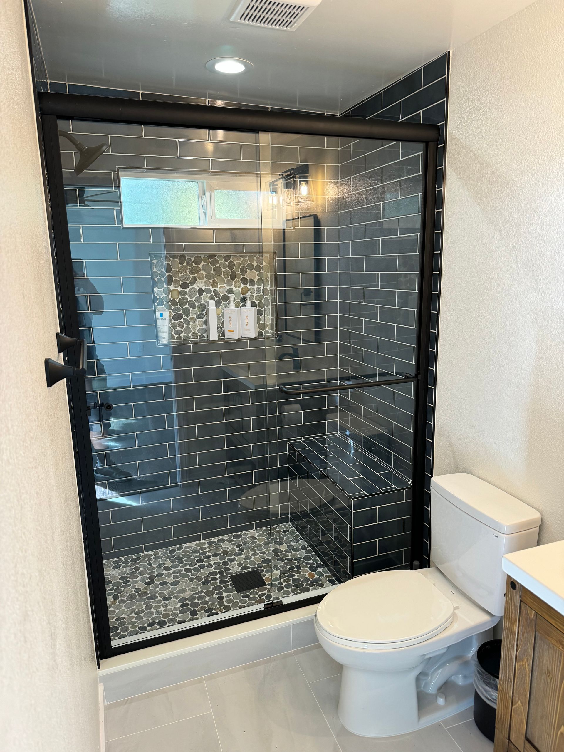 A bathroom with a toilet and a shower stall with a black frame.