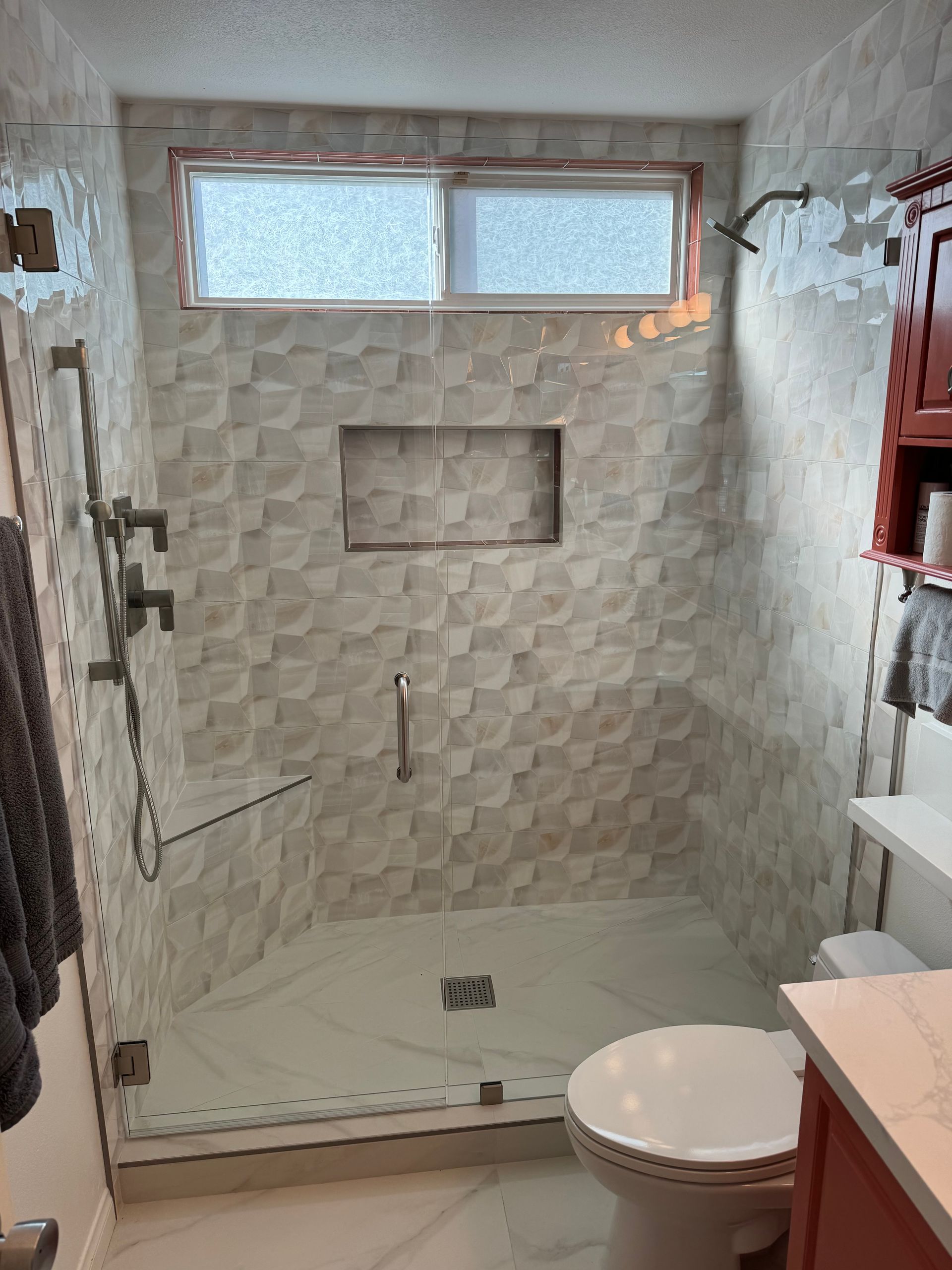 A bathroom with a walk in shower , toilet , sink and window.