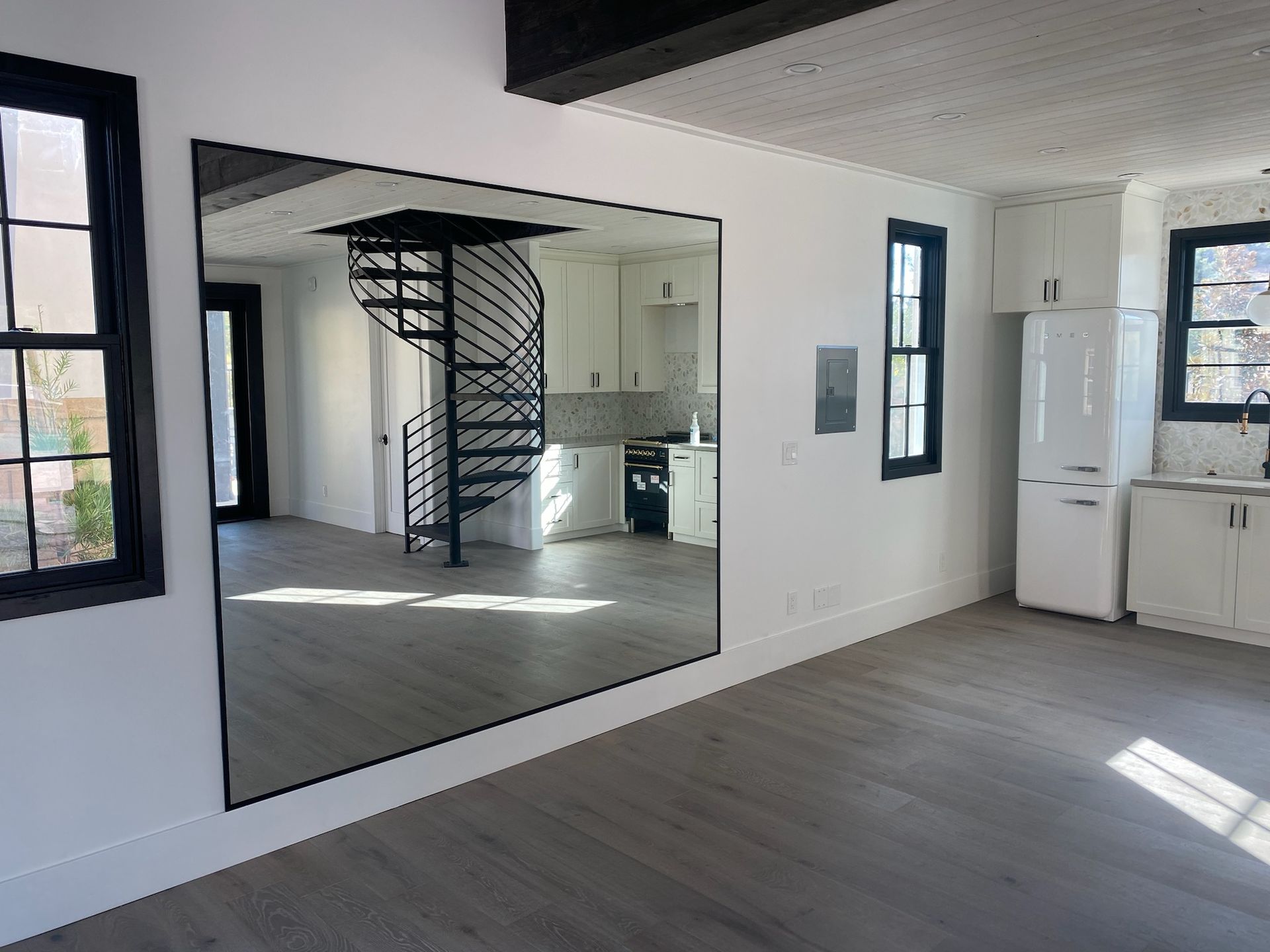 A living room with a large mirror on the wall and a spiral staircase in the background.
