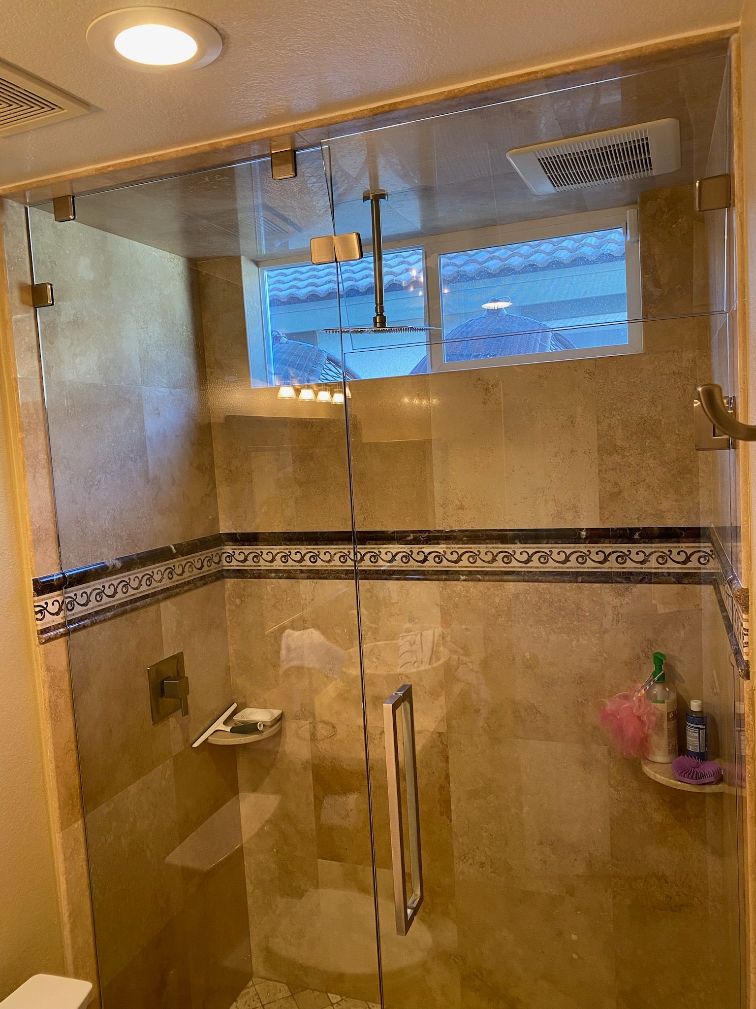 A bathroom with a walk in shower with a glass door and a window.