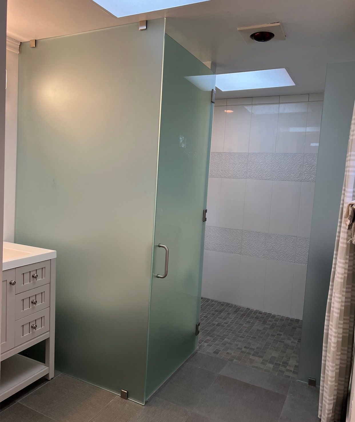 A bathroom with a glass shower door and a skylight.