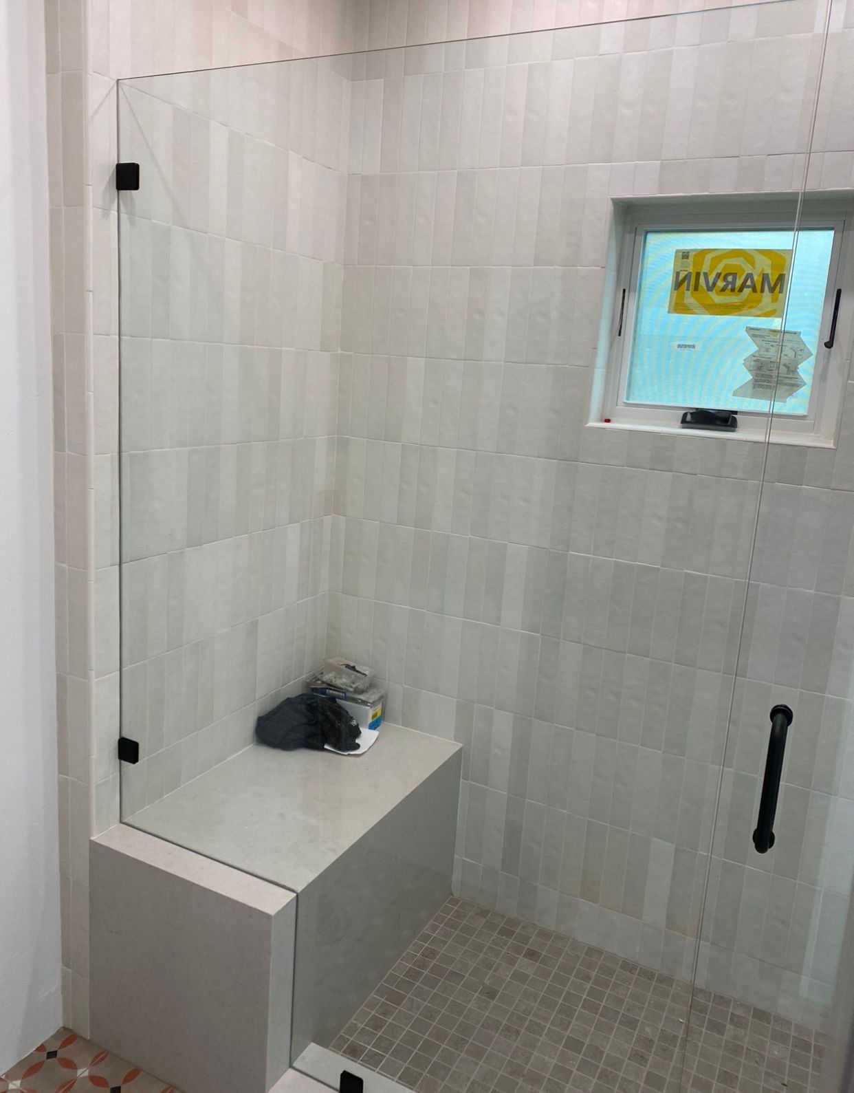 A bathroom with a walk in shower with a glass door and a window.