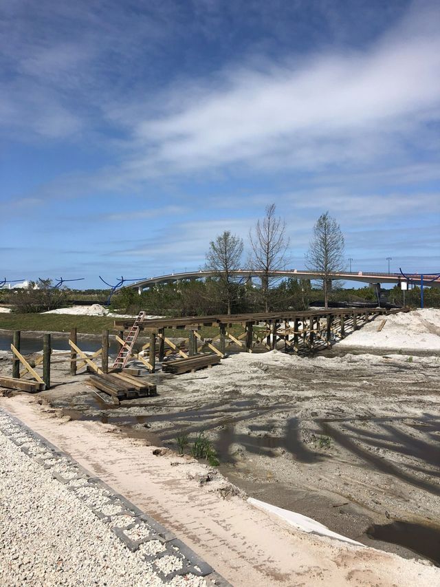 Sandy beach with wooden boardwalk, sparse trees, and blue sky with wispy clouds