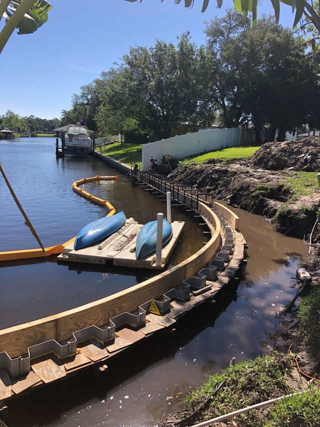 Curved dock on a canal with a blue kayak, water, and trees under a clear sky.