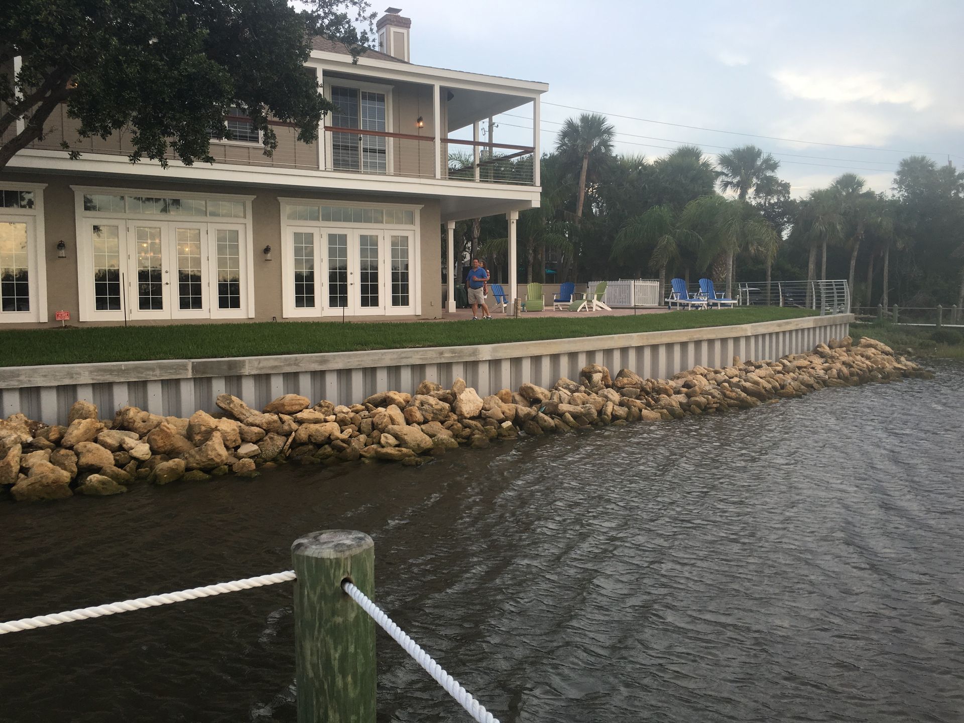 Waterfront house with white porch and rock shoreline beside choppy water