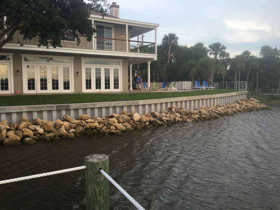 Waterfront house with white porch and rock shoreline beside choppy water