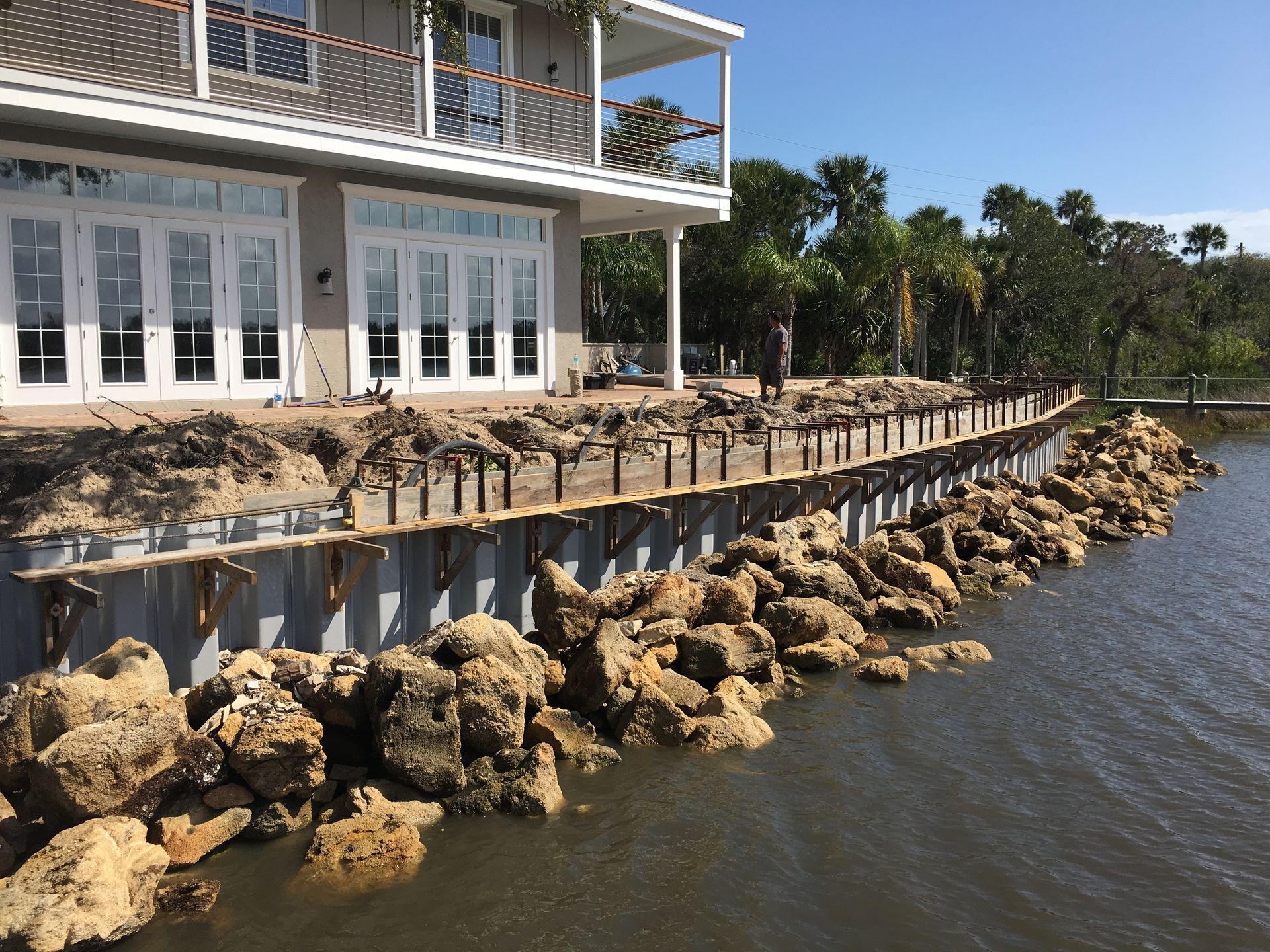 Coastal house with white balconies and a wooden walkway over rocky seawall beside the water
