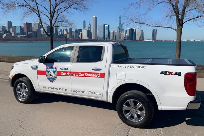 A white pickup truck with logo decals parked by a lake with the Chicago skyline in the background.