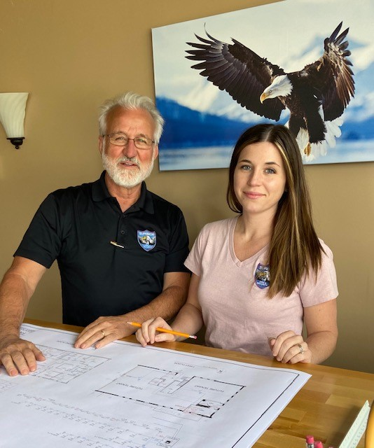 Two people reviewing architectural blueprints at a desk in front of a wall print of a bald eagle.