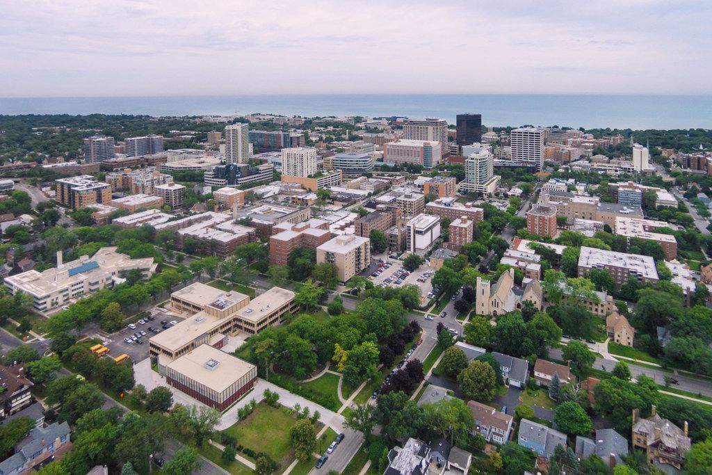 Aerial view of a city skyline with buildings and trees, transitioning to a horizon with a body of water.
