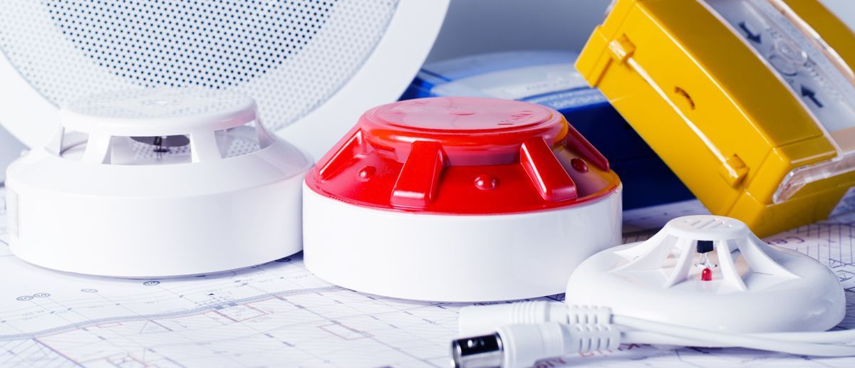 A selection of fire alarm system components, including smoke detectors, a red strobe light, and a yellow sounder.