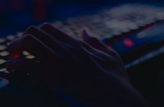 A person’s hand typing on a backlit mechanical keyboard in a dimly lit room.