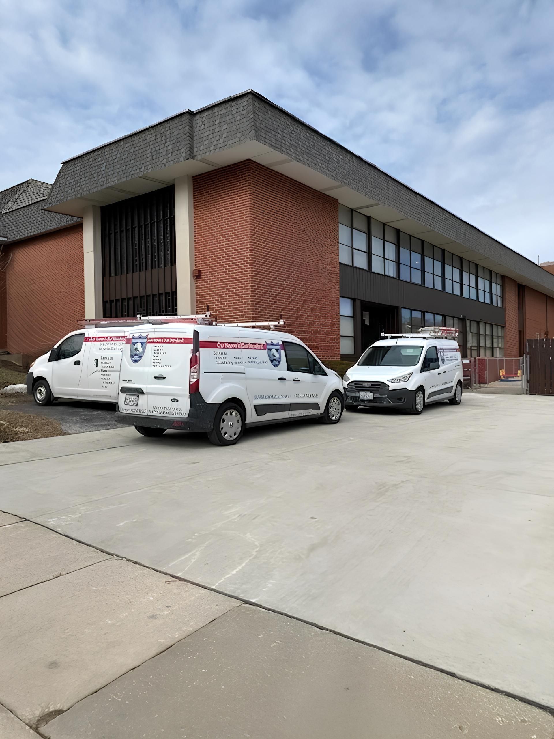White service vans parked outside a brick building with red paneling under a cloudy sky